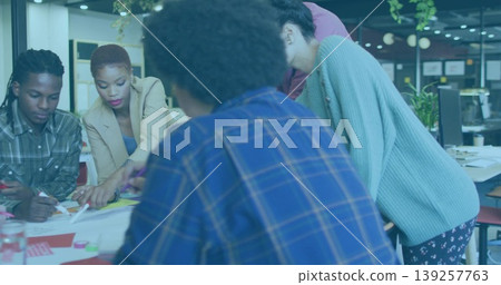 Leaning colleagues pointing and writing on large table at modern office, with papers and markers Leaning colleagues pointing and writing on large table at modern office, with papers and markers 139257763