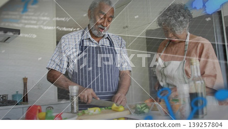 Chopping senior couple wearing aprons prepping fresh vegetables at kitchen counter, with knife Chopping senior couple wearing aprons prepping fresh vegetables at kitchen counter, with knife 139257804