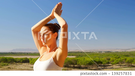 Practicing female yogi holding prayer pose in open scrubland wearing white tank top, copy space Practicing female yogi holding prayer pose in open scrubland wearing white tank top, copy space 139257831