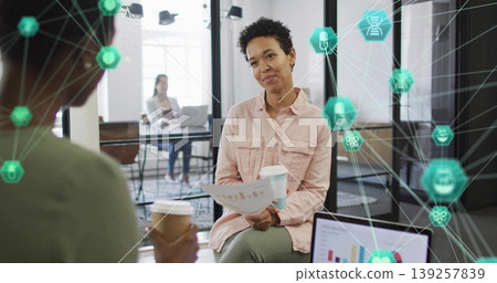 Discussing chart and sipping coffee curly-haired woman sitting in tech office showing data overlay Discussing chart and sipping coffee curly-haired woman sitting in tech office showing data overlay 139257839