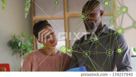 Examining woman in pink sweater and bearded man reviewing blue folder in office, with network icons Examining woman in pink sweater and bearded man reviewing blue folder in office, with network icons 139257840