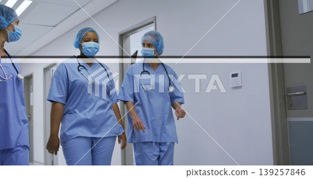 Walking medical staff in surgical caps and scrubs along hospital corridor, carrying stethoscopes Walking medical staff in surgical caps and scrubs along hospital corridor, carrying stethoscopes 139257846