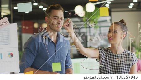 Teen girl drawing triangle with coworker watching on glass board in office, with sticky notes Teen girl drawing triangle with coworker watching on glass board in office, with sticky notes 139257949
