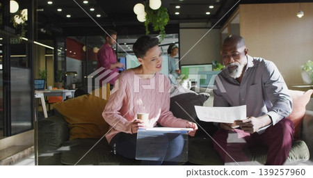 Reviewing paperwork mature colleagues sitting on dark sofa in modern office lounge, with coffee cup 139257960