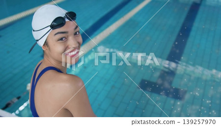 Smiling swimmer sitting at pool edge, white swim cap, dark blue swimsuit and goggles, copy space Smiling swimmer sitting at pool edge, white swim cap, dark blue swimsuit and goggles, copy space 139257970