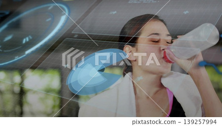 Pausing woman in sports top drinking from water bottle in studio with towel window bars holograms Pausing woman in sports top drinking from water bottle in studio with towel window bars holograms 139257994