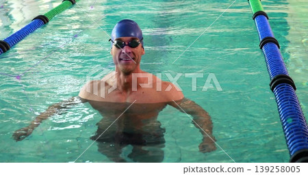 Standing male swimmer wearing cap and goggles in turquoise pool lane, with lane dividers 139258005