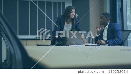Leaning professionals in formal attire discussing ideas in boardroom, with laptop, phone and papers Leaning professionals in formal attire discussing ideas in boardroom, with laptop, phone and papers 139258014