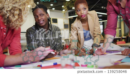 Collaborating professionals leaning over diagrams on office table with markers and chemical overlay Collaborating professionals leaning over diagrams on office table with markers and chemical overlay 139258046