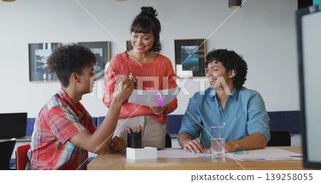Asian woman in red sweater standing at table in office, presenting printed charts with pen 139258055