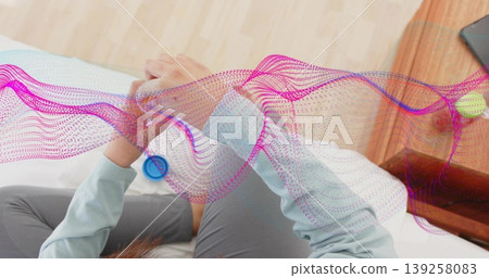 Checking Indian woman viewing fitness tracker in bed with smartphone green ball waveform graphics 139258083