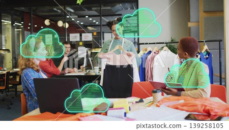 Holding pink-and-black dress, fashion designer standing at studio table, reviewing fabric swatches Holding pink-and-black dress, fashion designer standing at studio table, reviewing fabric swatches 139258105