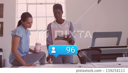 Collaborating designers reviewing blueprints at studio, with tablet, coffee cup and follower icon Collaborating designers reviewing blueprints at studio, with tablet, coffee cup and follower icon 139258111