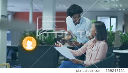 Reviewing printed document, colleagues sharing tablet sitting in office lounge chairs, chat overlay Reviewing printed document, colleagues sharing tablet sitting in office lounge chairs, chat overlay 139258131