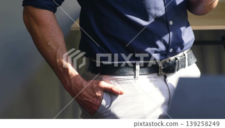 Standing mature male wearing navy shirt and beige trousers at office, showing black leather belt Standing mature male wearing navy shirt and beige trousers at office, showing black leather belt 139258249
