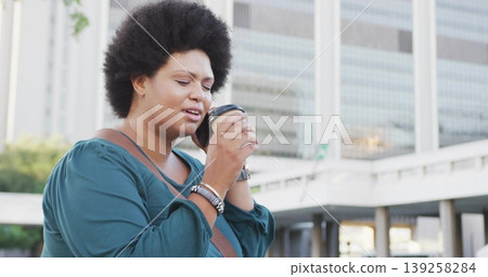 Woman in blouse holding disposable coffee cup near face in plaza, crossbody bag silver bracelets Woman in blouse holding disposable coffee cup near face in plaza, crossbody bag silver bracelets 139258284