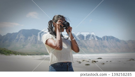 Framing photographer wearing white top and blue jeans, raising DSLR camera at shoreline with rocks Framing photographer wearing white top and blue jeans, raising DSLR camera at shoreline with rocks 139258285