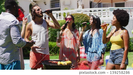Group of six friends grilling in backyard beside pool, with beer bottles, corn, sausages 139258286