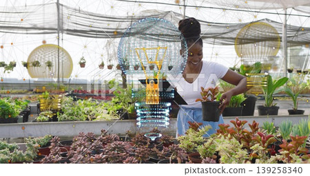 Greenhouse worker inspecting succulent on bench in shade with hanging pots using tablet hologram 139258340