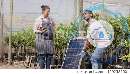 Coworkers installing solar panel in plant nursery, with tablet, work gloves, saplings and overlay 139258360
