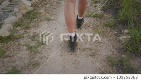 Walking person wearing black boots and white crew socks on gravel trail with grass, wooden boards Walking person wearing black boots and white crew socks on gravel trail with grass, wooden boards 139258369