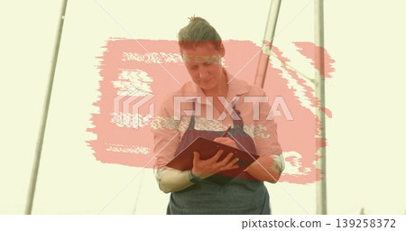 Writing notes gardener wearing blue apron in greenhouse metal poles with red notebook and pen Writing notes gardener wearing blue apron in greenhouse metal poles with red notebook and pen 139258372