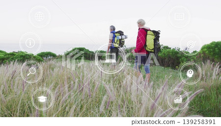 Walking couple wearing hiking gear along coastal dune footpath, with backpacks, rolled sleeping mat Walking couple wearing hiking gear along coastal dune footpath, with backpacks, rolled sleeping mat 139258391