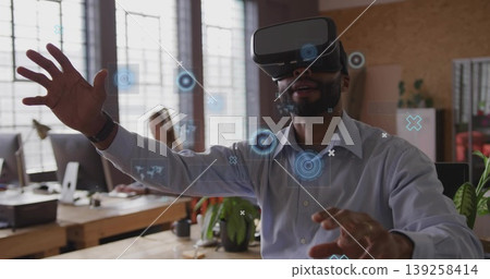 Reaching man wearing VR headset interacting with virtual interface at desk in office, copy space Reaching man wearing VR headset interacting with virtual interface at desk in office, copy space 139258414
