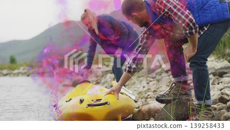 Friends steadying yellow kayak on rocky lakeshore using white-bladed paddle in pinkish-purple smoke Friends steadying yellow kayak on rocky lakeshore using white-bladed paddle in pinkish-purple smoke 139258433