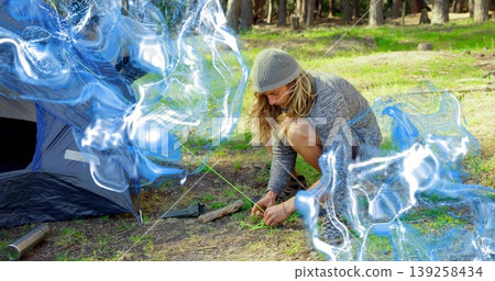 Securing camper fastening neon green guy line to tent stake in pine forest clearing, copy space 139258434