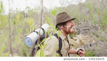 Crouching hiker wearing hat scanning hillside, with hiking backpack and trekking pole, copy space Crouching hiker wearing hat scanning hillside, with hiking backpack and trekking pole, copy space 139258435