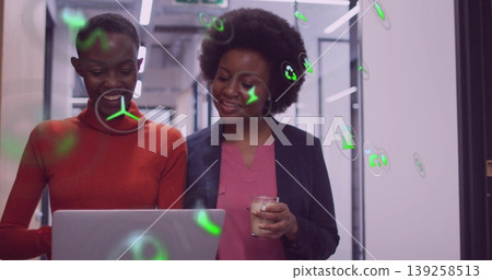 Two colleagues in red top and navy blazer examining laptop in office corridor, with AR icons Two colleagues in red top and navy blazer examining laptop in office corridor, with AR icons 139258513