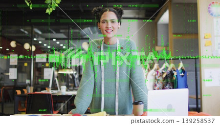Designer in green sweater smiling and measuring fabrics in studio, with laptop and measuring tape 139258537