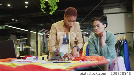 Collaborating designers marking fabric on table in design studio, with measuring tape and scissors 139258548