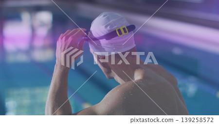 Male swimmer adjusting purple goggles with yellow clip and wearing white swim cap in lap pool Male swimmer adjusting purple goggles with yellow clip and wearing white swim cap in lap pool 139258572