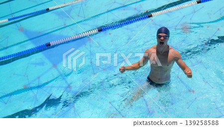 Emerging male swimmer raising fists from lane dividers in blue water, with swim cap goggles briefs 139258588