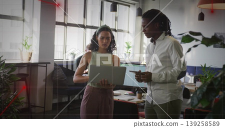 Reviewing laptop screen, two coworkers standing in open-plan office, with dual monitors, plants Reviewing laptop screen, two coworkers standing in open-plan office, with dual monitors, plants 139258589