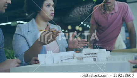 Presenting woman architect wearing blazer, gesturing with pencil at model in studio, with coworkers Presenting woman architect wearing blazer, gesturing with pencil at model in studio, with coworkers 139258600