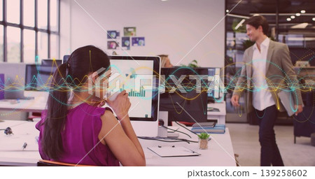 Drinking mature adult woman analyzing graphs on computer at open-plan office desk, with ceramic mug Drinking mature adult woman analyzing graphs on computer at open-plan office desk, with ceramic mug 139258602