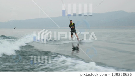 Gliding man wearing neon life vest on wakeboard across lake, gripping tow rope amid boat wake Gliding man wearing neon life vest on wakeboard across lake, gripping tow rope amid boat wake 139258626
