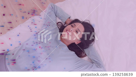 Lying Indian woman wearing casual top and gray pants on white sheets in bedroom, with pillow 139258639