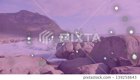 Crashing waves hitting granite boulders on shoreline, rising mountain ridge and floating light orbs Crashing waves hitting granite boulders on shoreline, rising mountain ridge and floating light orbs 139258643