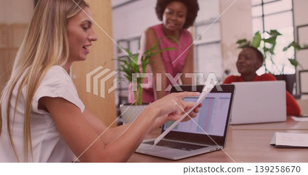 Pointing worker wearing white blouse examining printout on laptop at office with plant, copy space 139258670