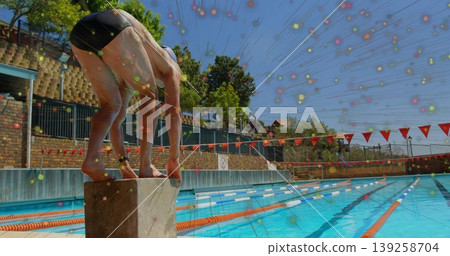 Crouching swimmer gripping starting block at lap pool, with lane ropes and flags, copy space 139258704