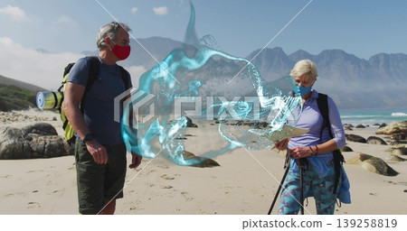 Mature couple scanning digital swirl on sandy shore with backpacks poles map and masks Mature couple scanning digital swirl on sandy shore with backpacks poles map and masks 139258819