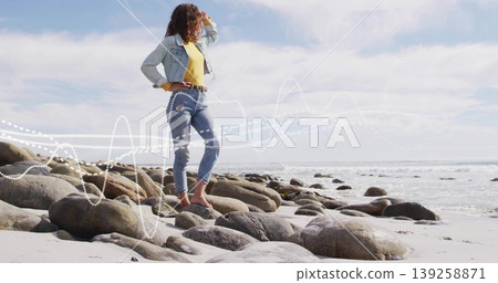 Shading eyes, woman wearing denim jacket cuffed jeans gazing across beach rocks, waves, copy space Shading eyes, woman wearing denim jacket cuffed jeans gazing across beach rocks, waves, copy space 139258871