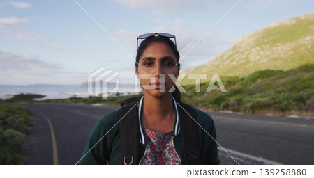 Standing traveler wearing jacket, sunglasses on winding asphalt road by sea, with backpack straps Standing traveler wearing jacket, sunglasses on winding asphalt road by sea, with backpack straps 139258880