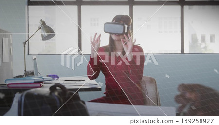 Reaching out worker wearing red dress VR headset at office, engaging VR interface with laptop Reaching out worker wearing red dress VR headset at office, engaging VR interface with laptop 139258927