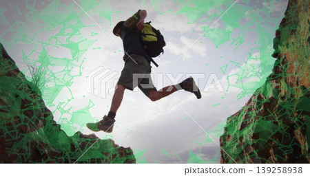 Leaping man in wide-brimmed hat, hiking boots and backpack across rugged rock gap in desert canyon 139258938