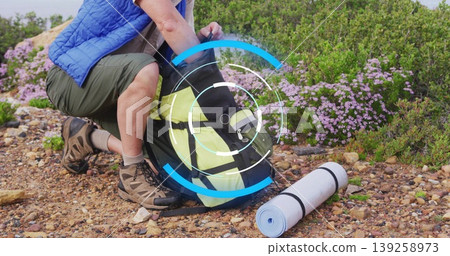 Unpacking male hiker wearing blue vest organizing backpack on hillside, with rolled sleeping mat Unpacking male hiker wearing blue vest organizing backpack on hillside, with rolled sleeping mat 139258973